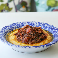 Load image into Gallery viewer, A bowl of organic beef bourguignon served over polenta, garnished with herbs.
